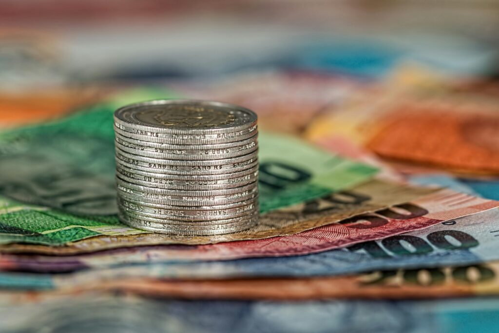 pexels-photo-210574-210574 A stack of coins on top of various colored banknotes, symbolizing finance and currency.